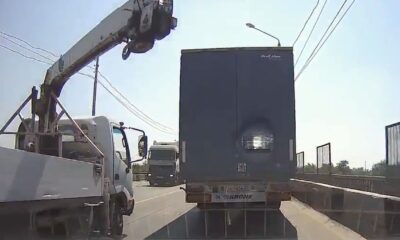 The crane hanging on the moving truck on the highway hit the truck trailer